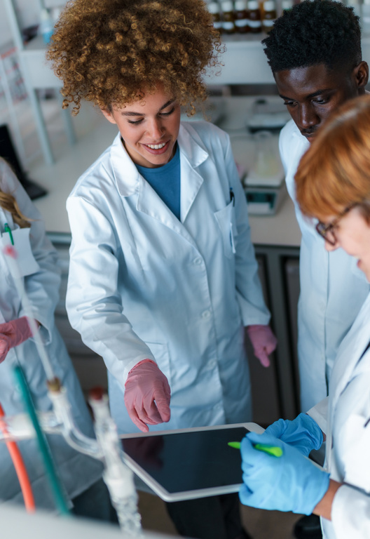 Gruppe von unterschiedlichen jungen Studenten der Naturwissenschaften und ihrem Professor, die während eines Experiments in einem modernen Labor zusammenarbeiten, ein digitales Tablet benutzen und Notizen machen