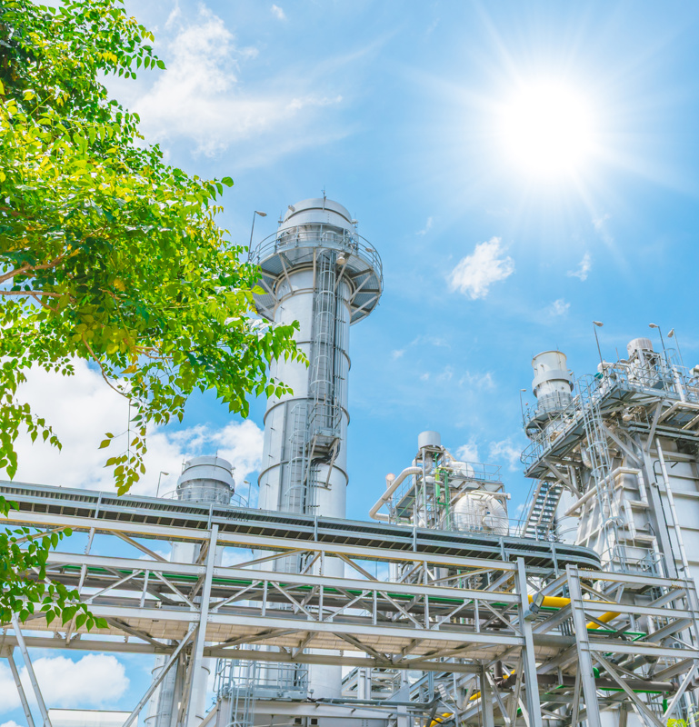 Modernes Konzept für eine nachhaltige Energiewirtschaft. Kraftwerk unter blauem Himmel hinter einem Baum.